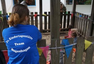 Eine junge Frau mit blauem Shirt steht mit dem Rücken zur Kamera