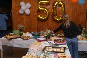 Eine goldene 50 aus Luftballons hängt an einer Wand, im Vordergrund weiß gedeckte Tische auf denen Essen steht